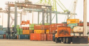 Terminal kargo yang sibuk di Pelabuhan Makassar dengan kontainer dan derek, suasana industri yang semarak.